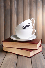 Cup with mustache on table on wooden background
