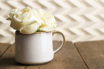 Beautiful white roses in cup on wooden table