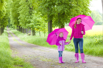 mother and her daughter with umbrellas in spring alley