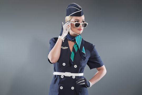 Smiling retro blonde stewardess wearing blue suit. Wearing white