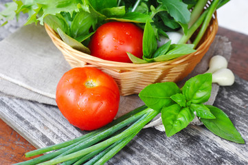 Fresh vegetables and greenery are in a basket on a old wooden