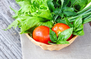 Fresh vegetables and greenery are in a basket on a old wooden