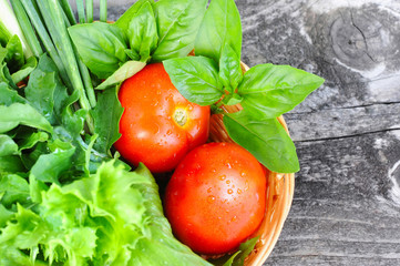 Fresh vegetables and greenery are in a basket on a old wooden