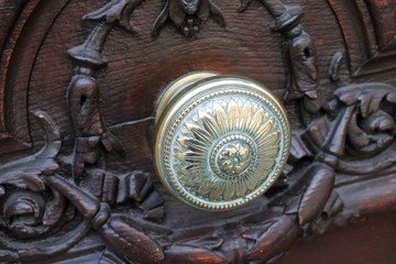 Ornate brass knob set in a massive carved wooden door