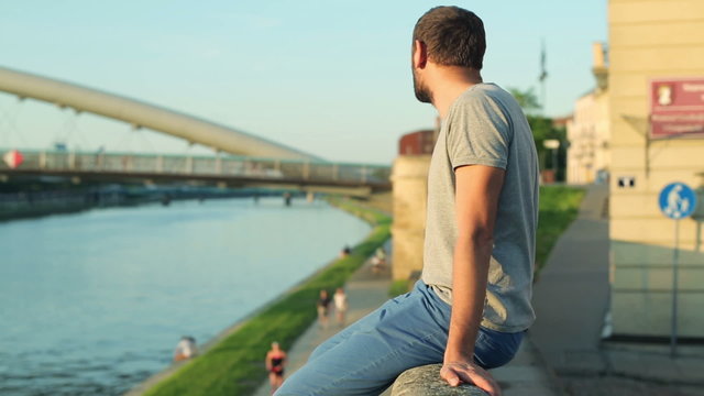 Young sad, depressed man sitting on the wall by the river