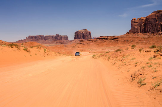 Dirt Road Through Monument Valley with a Vehicle in Distance