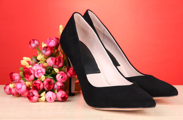 Beautiful black female shoes and flowers on red background