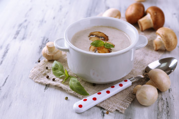 Mushroom soup in white pot, on napkin, on wooden background