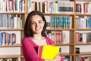 Happy female student holding books at the library