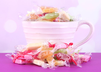 Tasty candies in mug on table on bright background