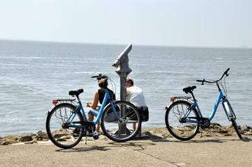 Eine Fahrradpause an der Nordsee und auf das offene Meer schauen. Zwei Frauen sitzen am Ufer  mit...