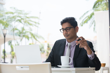 young indian business male on laptop and coffee at a cafe