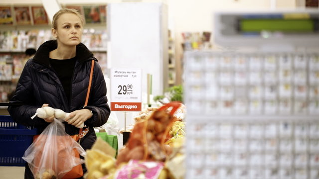 Young woman shopping in supermarket and choosing vegetables