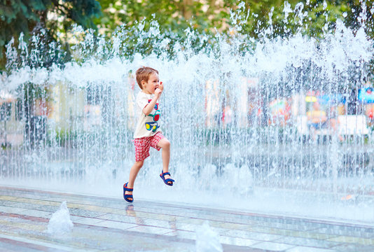excited boy running between water flow in city park