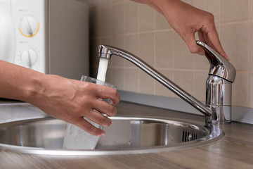 Woman, pouring water from faucet into a glass at a kitchen