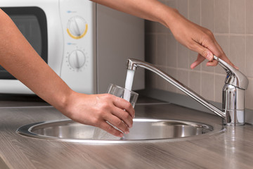 Woman, pouring water from faucet into a glass at a kitchen
