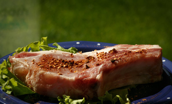 Raw pork steak sprinkled with pepper on blue plate with salad