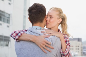 Hip young couple hugging with woman kissing his cheek