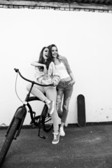Two hipster girl friends  with skateboard and bicycle.