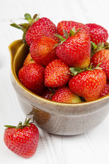 Fresh organic strawberries in bowl on white wooden background