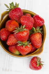 Fresh organic strawberries in bowl on white wooden background