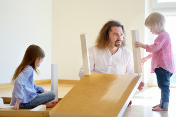 Father and his two daughters assembling a table - obrazy, fototapety, plakaty