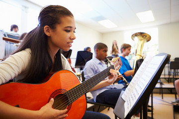 Female Pupil Playing Guitar In High School Orchestra - Powered by Adobe
