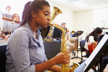 Female Pupil Playing Saxophone In High School Orchestra - obrazy, fototapety, plakaty