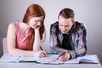 Teenage couple drawing hearts instead of learning