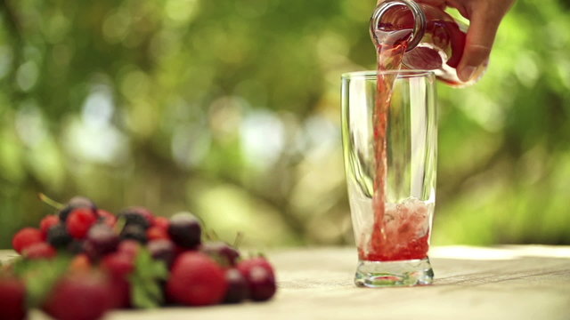 A person pouring berry fruit juice in glass in slow motion