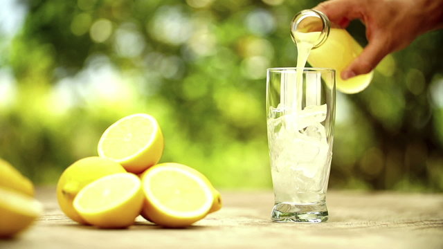 Fresh lemon juice being poured into glass with lemons on outdoor table