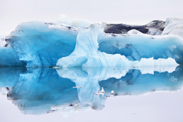 Fototapeta na wymiar Blue iceberg symmetrically reflected in the water in the ice lagoon Jokulsarlon, Iceland