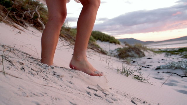Girl walking through beach dunes at sunset