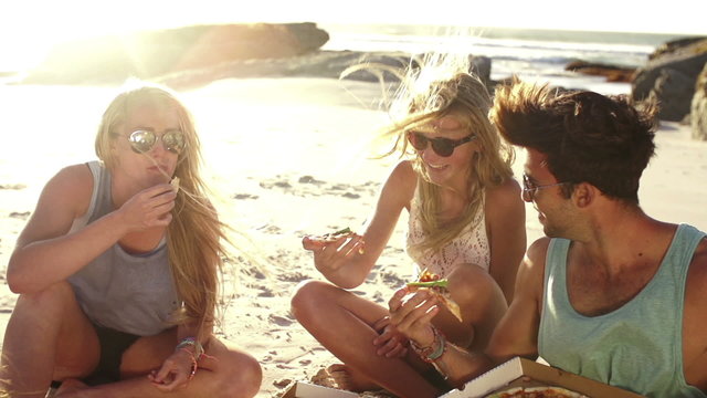 Friends eating pizza on beach
