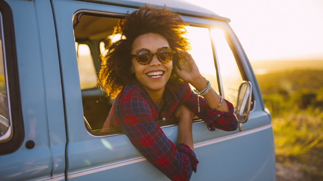 Woman in vintage car laughing at sunset