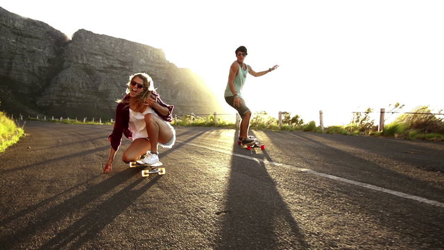 Friends longboard skating on road sunset