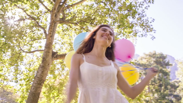 woman walking with colorful balloons in park