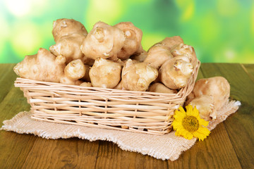 Topinambur roots in wicker basket on table on bright background
