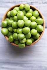 Green peas in wooden bowl on wooden background