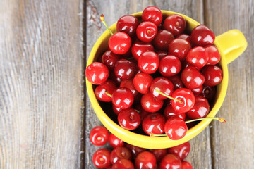 Sweet cherries in mug on wooden background
