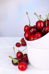 Ripe sweet cherries in cup on wooden table