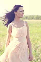 Naklejka na ściany i meble Beautiful woman in pink dress standing in a field