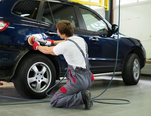 Serviceman polishing car body with machine  in a workshop