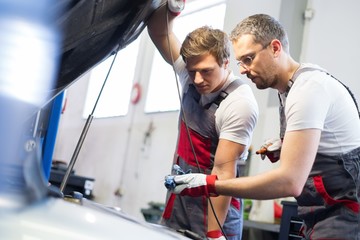 Two mechanics checking oil level in a car workshop