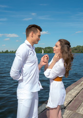 Guy holds the girl's hand on a wooden pier near the water.