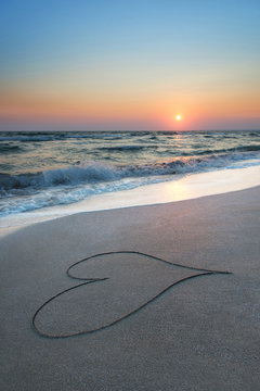 heart outline on beach sand against sea and sunset