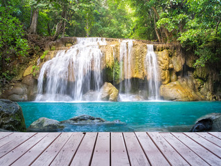 Fototapeta na wymiar Waterfall, green forest in Erawan National Park in Thailand montage with wooden floor. Landscape with water flow, tree, river, stream and rock at outdoor. Beautiful scenery of nature for vacation.