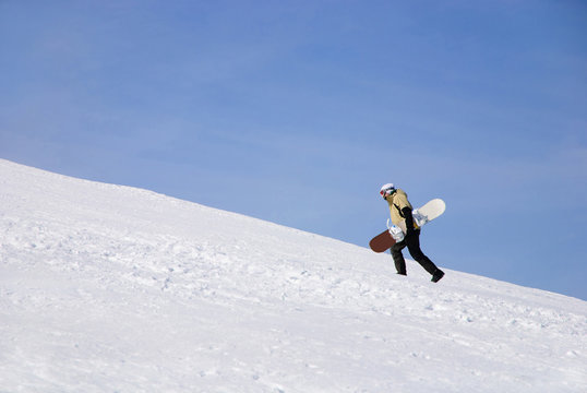 snowboarder walking against snowy mountains and blue sky