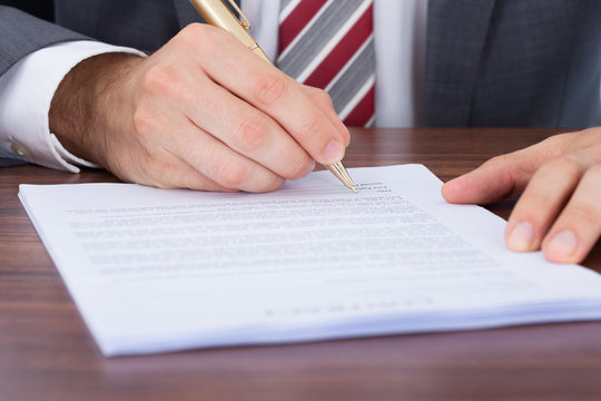 Businessman Signing Document At Desk