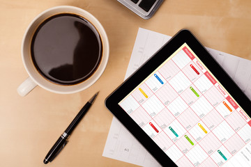 Tablet pc showing calendar on screen with a cup of coffee on a d